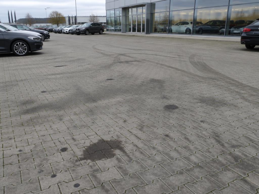 Verschmutzte Autohaus-Vorfläche mit Öl- und Reifenabdrücken